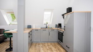 Una cocina moderna con gabinetes grises, una encimera de madera y un horno empotrado. Hay un ventanal sobre el fregadero y otro a la izquierda.