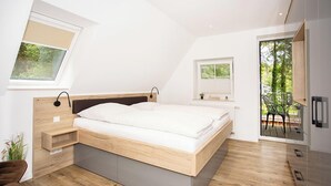 Un dormitorio moderno con una cama de madera, mesitas de noche empotradas, un ventanal pequeño y un balcón con una silla.