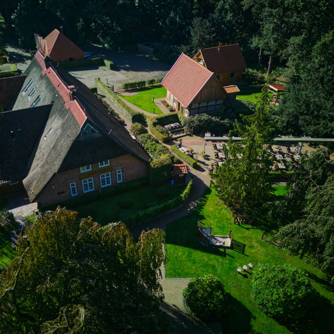 Un edificio de estilo europeo tradicional con un tejado empinado, rodeado de exuberante vegetación y un jardín cuidado.