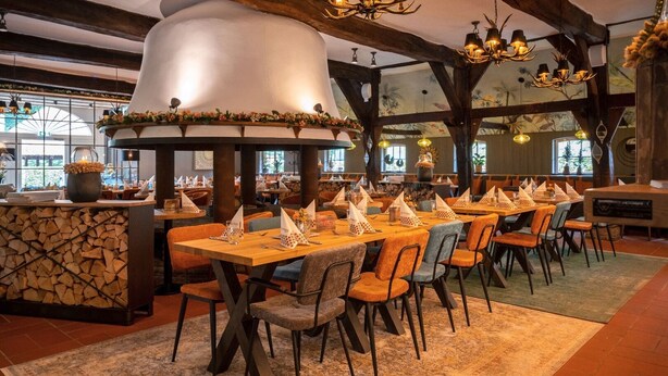 Ein Restaurant mit langen Holztischen, orangefarbenen und grauen Stühlen und einem großen Ziertefeuerrohr.