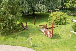 A well-maintained garden with wooden play structures, a large tree, and a neatly trimmed bush.
