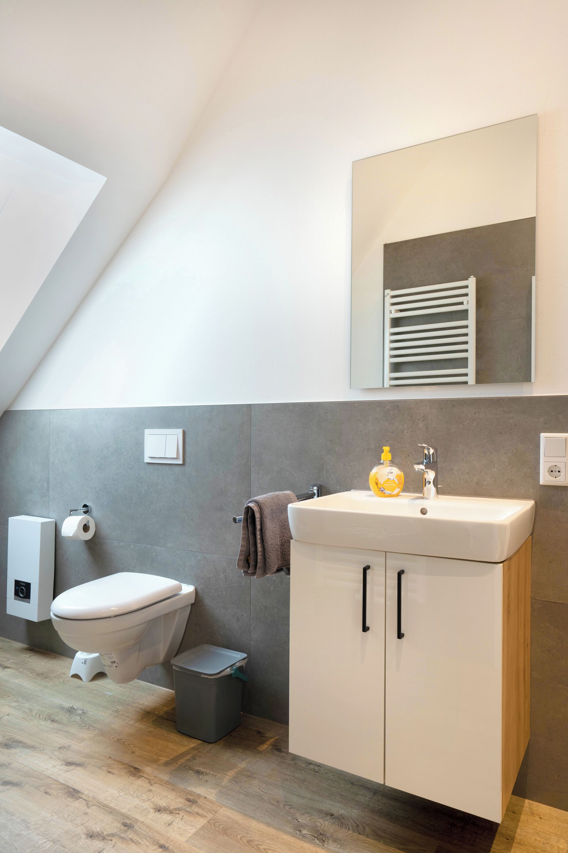 Une salle de bain moderne avec des toilettes blanches, un lavabo doté d’un distributeur de savon et une serviette accrochée au mur.