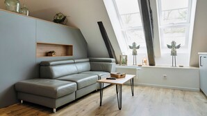 Ein modernes Wohnzimmer mit einem grauen Ecksofa, einem Holztisch und einem großen Fenster mit Blick auf Bäume.