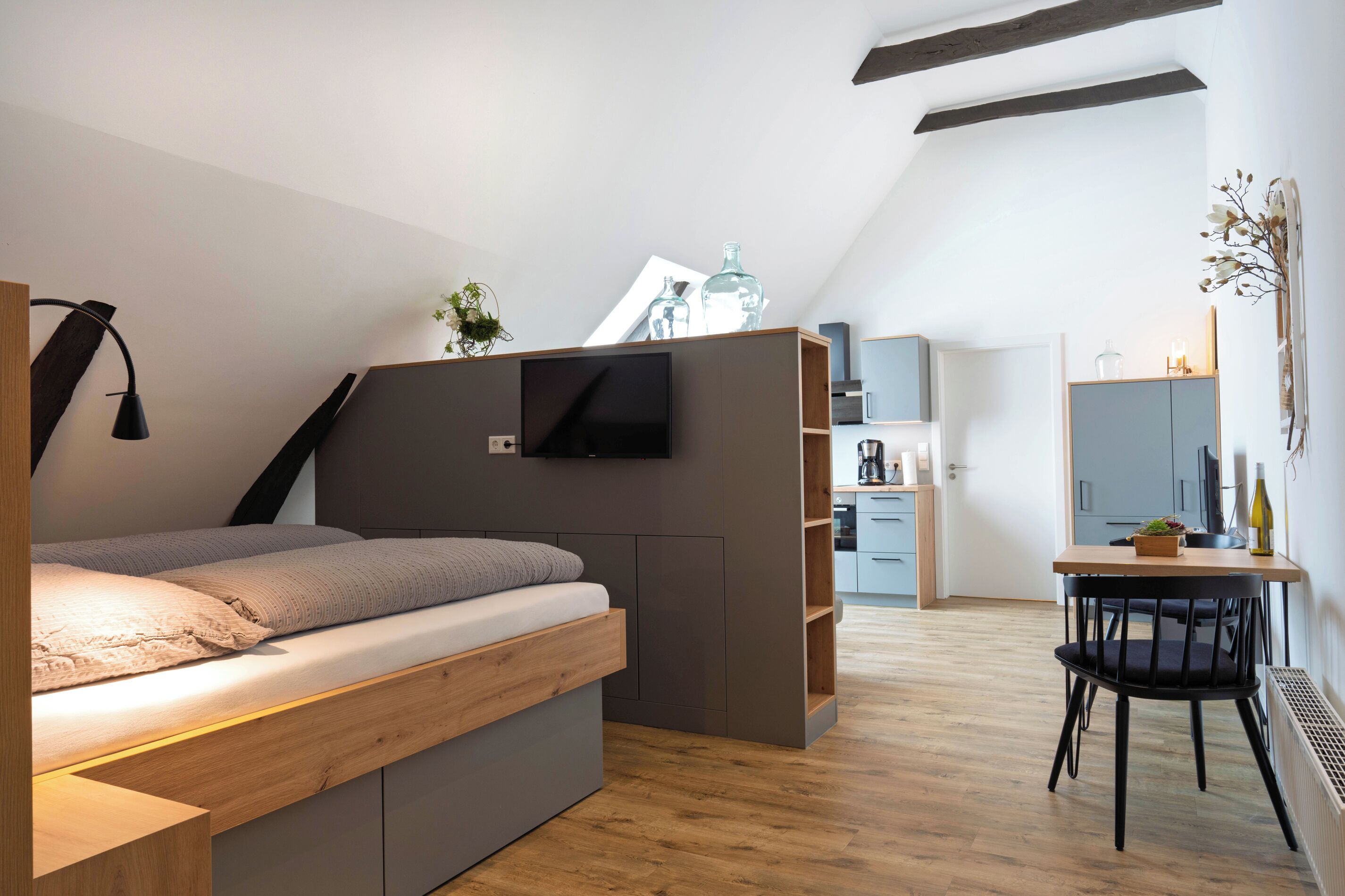 A modern bedroom with a loft bed, built-in TV, and a small dining area.
