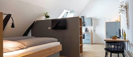 A modern bedroom with a loft bed, built-in TV, and a small dining area.