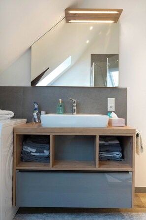 Un bagno moderno con un mobile bagno in legno, un lavandino bianco e uno specchio grande. Sul mobile ci sono asciugamani e articoli da toilette.