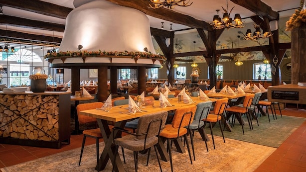 A restaurant with long wooden tables, orange and gray chairs, and a large decorative chimney.