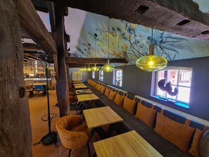 Un ristorante con lunghe tavole di legno e panche imbottite color arancio, un affresco sulla parete e lampade gialle pendenti.