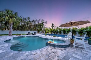 Ein Swimmingpool mit Whirlpool, umgeben von Palmen und einem weißen Zaun.
