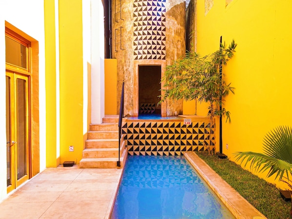 A narrow alley with a pool, yellow walls, and geometric tile patterns.