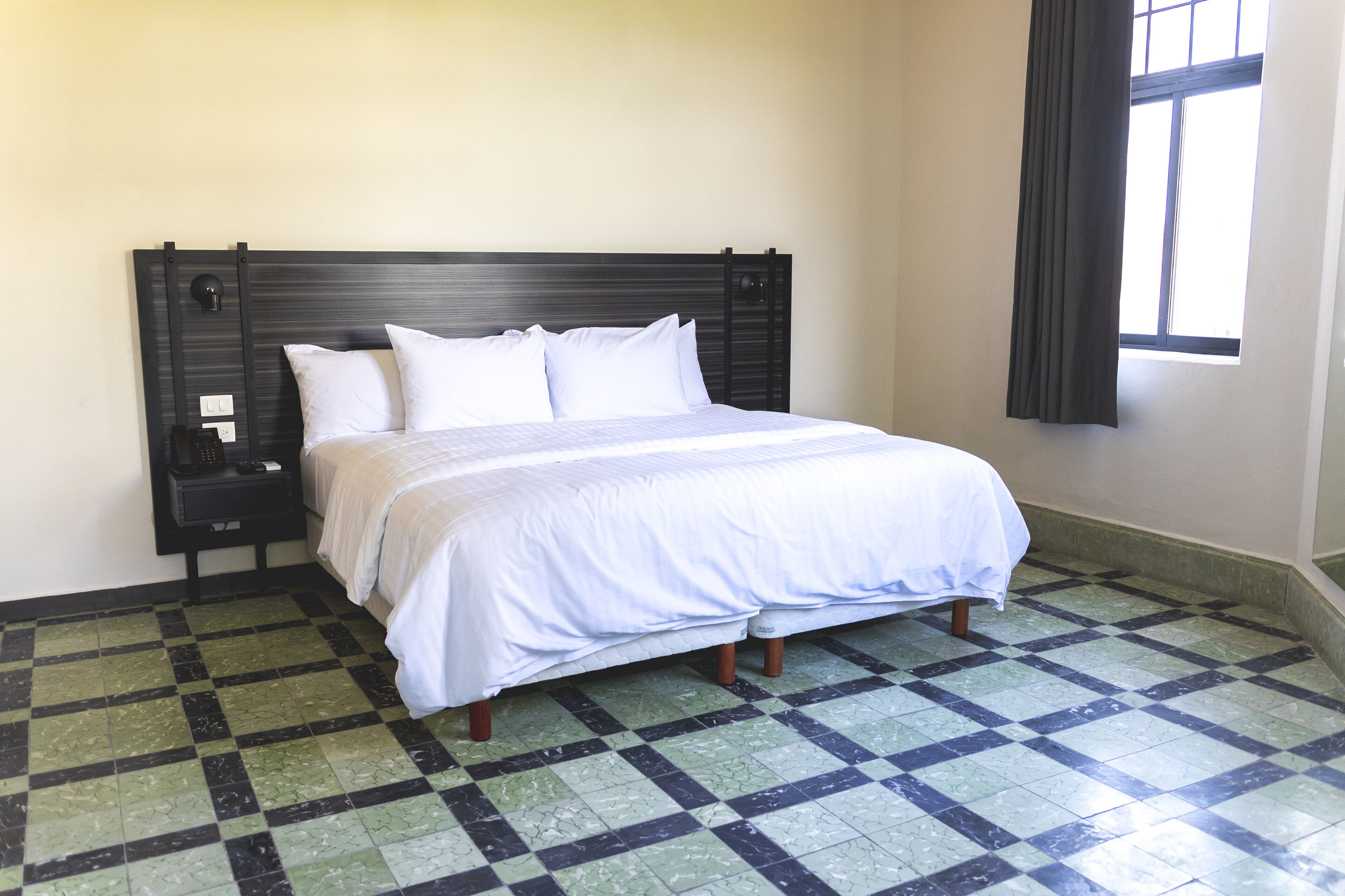 A neatly made bed with white linens in a room with a checkered floor and a dark headboard.