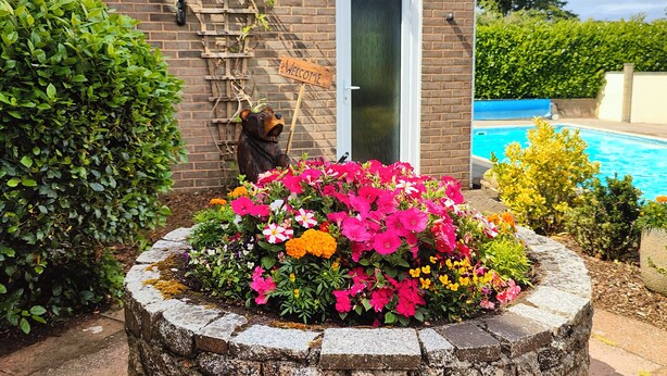 A brick building with a welcome sign, a bear decoration, and a flower bed in front.