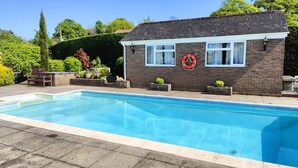 A swimming pool with a brick house in the background, a lifebuoy on the wall, and a bench.