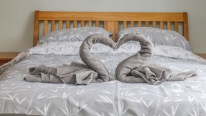 A bed with a wooden headboard, grey floral bedding, and two towels arranged in a swan shape.