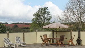 A patio with a table and chairs, a wooden stove, and a large tree.