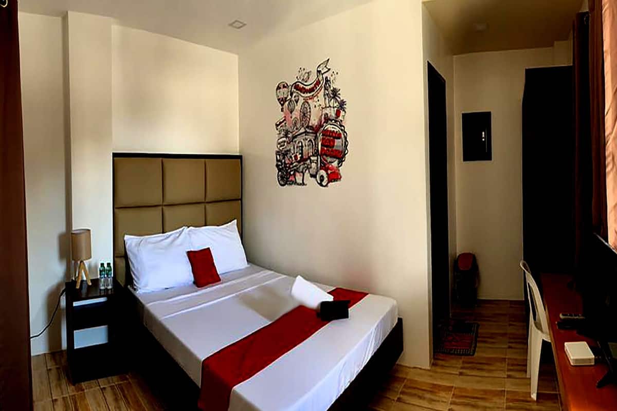 A hotel room with a bed, a nightstand, a desk, and a wall decoration.