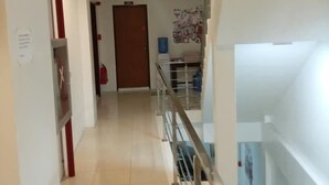 A corridor with a tiled floor, a door at the end, and a staircase with a glass railing. - OYO 869 Jnv Dream Hotel (Subic)