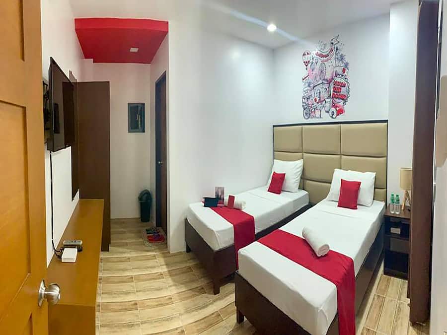 A hotel room with two beds, a red ceiling, a wall art piece, and a wooden floor.