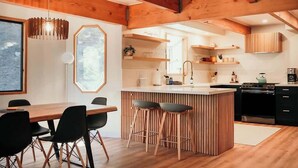 Una cocina moderna con vigas de madera, una isla central con taburetes y un comedor con mesa y sillas.