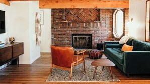 Una sala de estar acogedora con chimenea de ladrillo, vigas de madera en el techo, un sofá verde y un sillón de cuero.