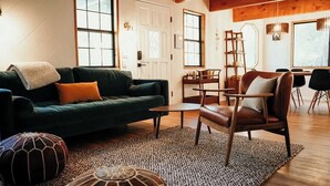 Un salón acogedor con un sofá verde, un sillón de cuero marrón y una alfombra tejida.