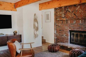 A living room with a brick fireplace, wooden beams, a leather sofa, and a flat-screen TV.