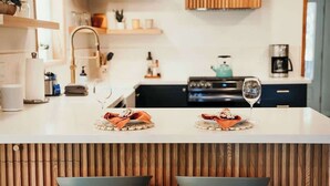 Una cocina moderna con encimera blanca, dos taburetes y una copa de vino.