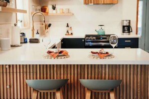 A modern kitchen with a white countertop, two stools, and a wine glass.