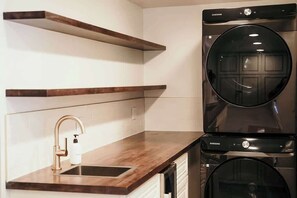 A modern kitchen with a built-in washer and dryer, a stainless steel sink, and wooden shelves.