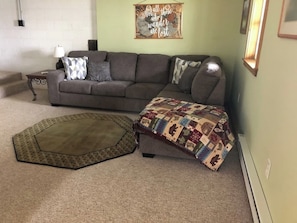 Un salon avec un canapé gris, un tapis à motifs et une courtepointe posée sur le sol.