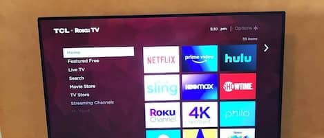 Un televisor TCL Roku sobre un mueble de madera con un reloj encima.