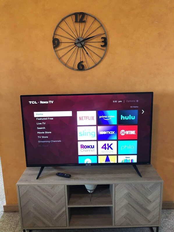 A TCL Roku TV on a wooden TV stand with a clock above it.