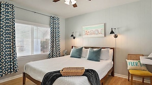 A bedroom with a bed, a ceiling fan, a bedside table, a chair, and a window with blinds.