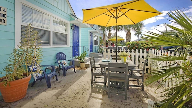 A turquoise building with a white picket fence, outdoor seating, and a yellow umbrella.