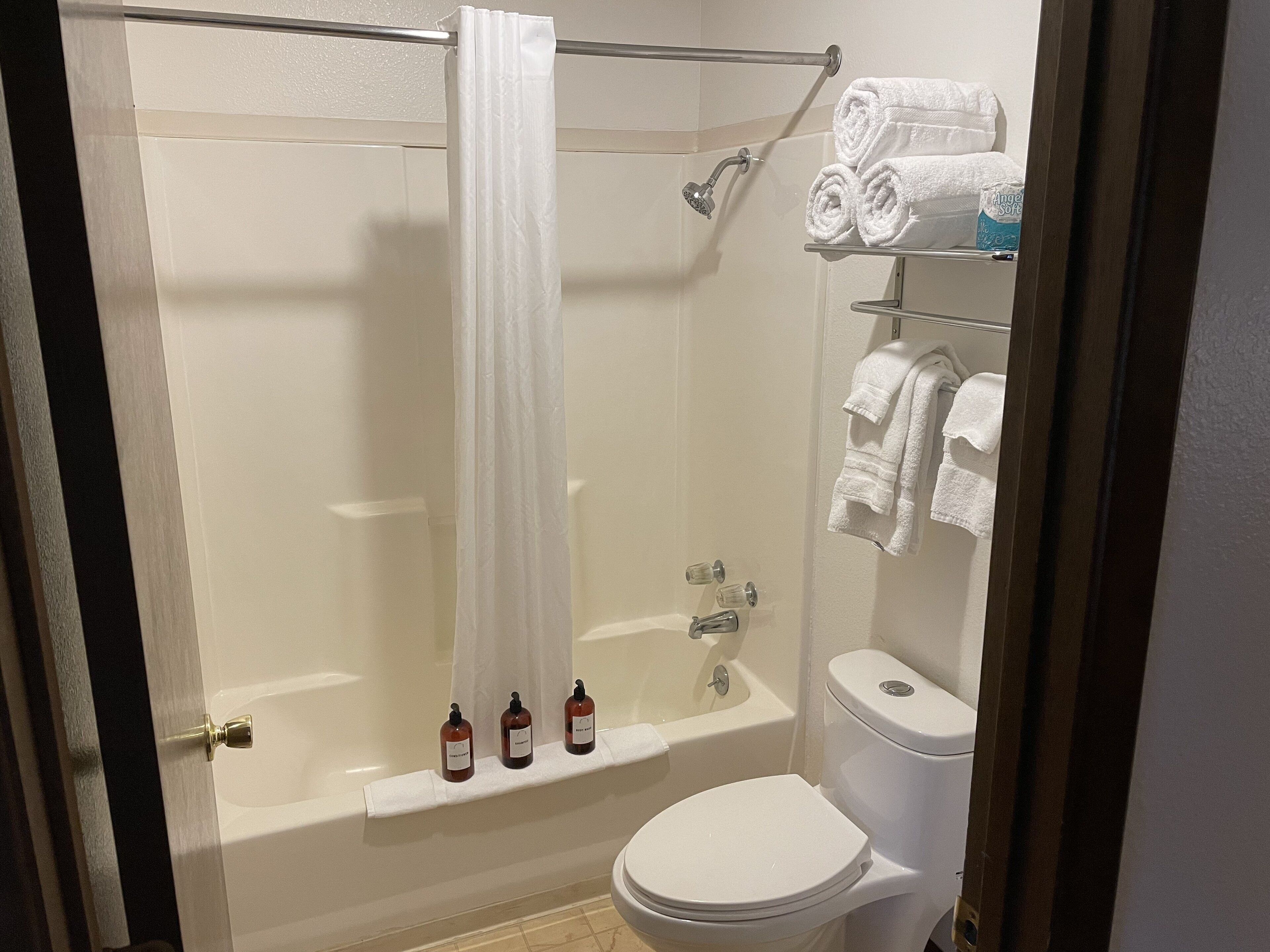 A bathroom with a glass-enclosed shower, a white toilet, and a shelf with rolled towels and toiletries.