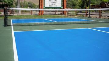 Una cancha de tenis con red, rodeada por un letrero de River's Fork Lodge.