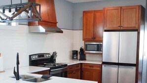 A modern kitchen with wooden cabinets, stainless steel appliances, and a central island with bar stools. - Unique 3BR Home with great views Beach Access (Atlantic Beach)