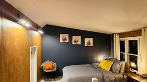 A bedroom with a bed, a chair, and artwork on the wall.