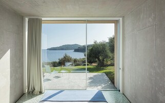 Una habitación con un amplio ventanal corredera que da a un balcón con vistas a un lago y colinas.
