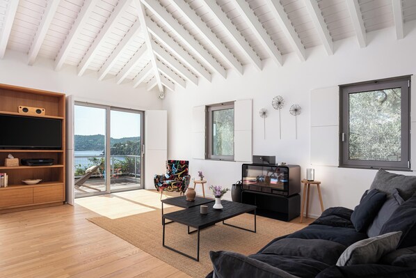 A modern living room with a large TV, a sofa, a coffee table, and a view of the outdoors.