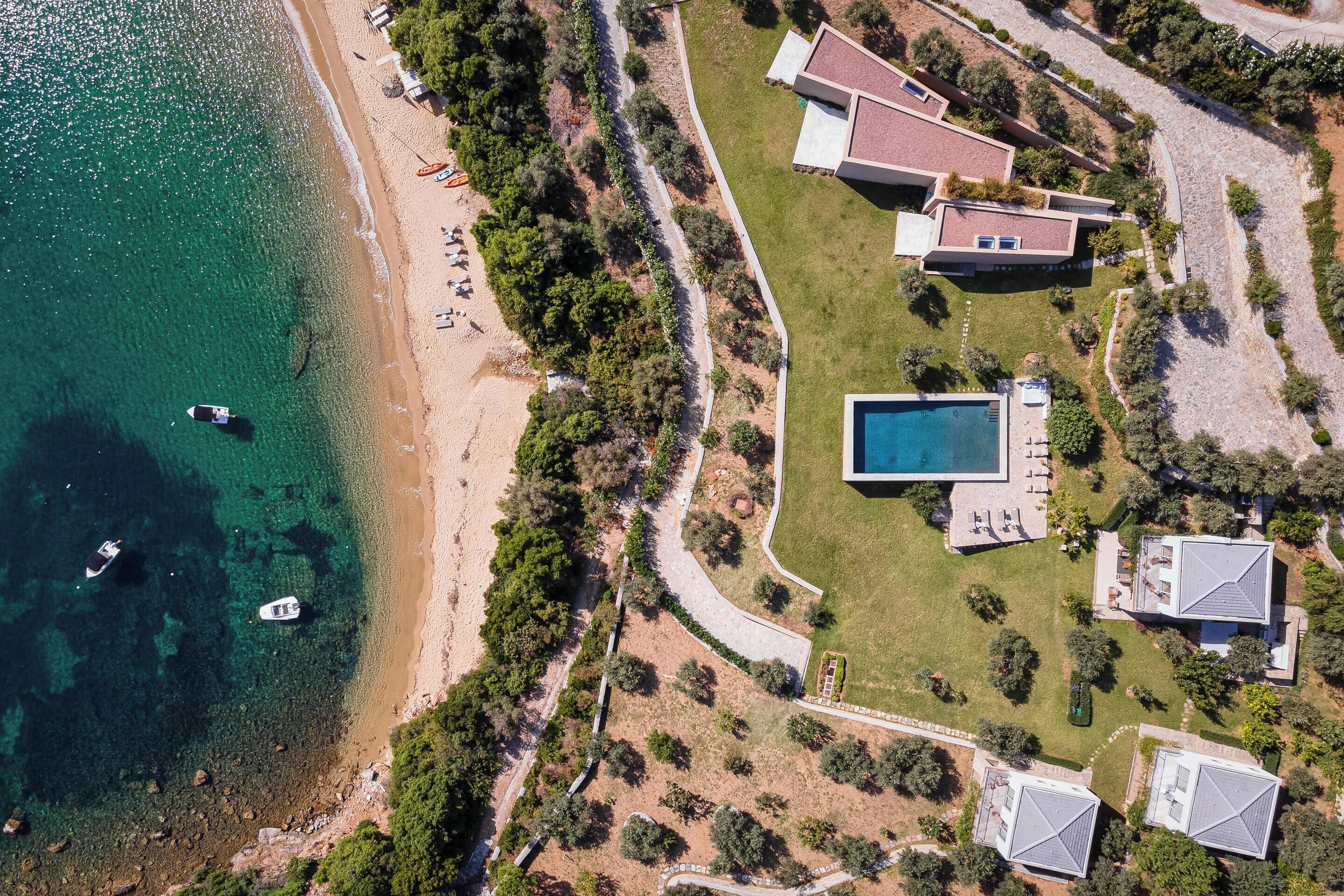 Vista aérea de una propiedad costera con piscina, varias casas y una playa.