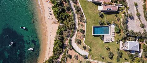 Vista aérea de una propiedad costera con piscina, varias casas y una playa.
