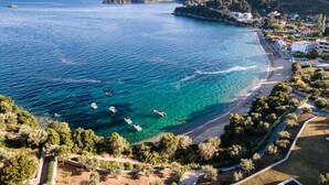 Zona costera con aguas azules cristalinas, embarcaciones y una playa con edificios y vegetación.