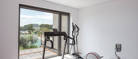 A modern room with a treadmill, elliptical, and stationary bike, large windows with a view of a deck and greenery.