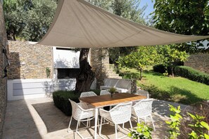 A patio with a wooden table and white chairs, a stone wall, and a large tree. - Pelagoon Skiathos (Skiathos)