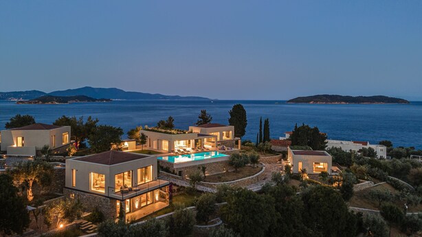 Una propiedad costera con varias casas modernas, una piscina y vistas al mar y a islas distantes.