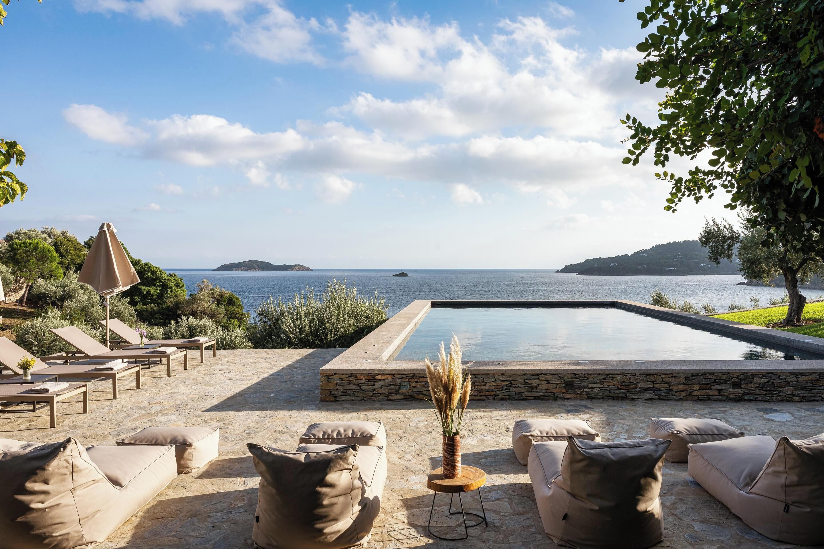 Zona de piscina con sillones reclinables y vista al mar.