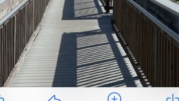 Une promenade en bois menant à une plage où l’on aperçoit, au loin, des parasols et des gens.