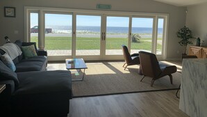 Un salon spacieux doté d’une grande porte-fenêtre coulissante donnant sur un balcon avec vue sur la plage.