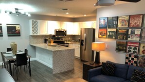 A modern kitchen with granite countertops, stainless steel appliances, and a central island. There is a dining area with a table and chairs, and a living room with a sofa and a coffee table. - Amazing Five-Star Luxury Thornton Park two Bedroom Apt - close to Kia Center. (Orlando)